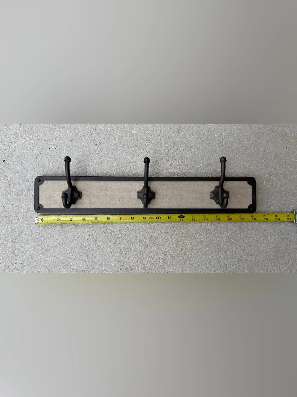 Hook rack features a dark bronze frame with a light-colored linen backing